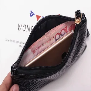 Black crocodile pattern clutch bag holding a smartphone and cash for size reference