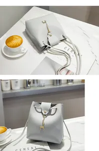 Detail van lichtgrijze emmer-tas met gouden hertenhanger op marmer met koffie en tijdschrift
