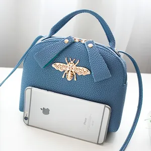 Blue lychee leather crossbody bag with bee ornament shown next to a smartphone
