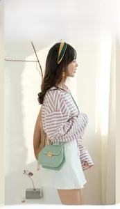 Detail of mint green crossbody bag with golden round buckle and decorative stitching