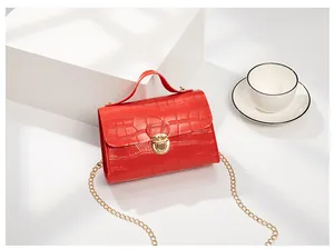 Detailed view of red crocodile pattern handbag with golden rotary lock and chain strap