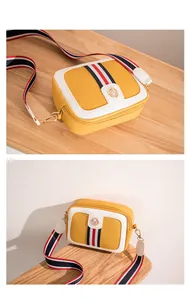 Close-up of yellow and white leather camera bag with striped ribbon and gold logo
