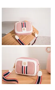 Pink and white cross-body camera bag with colorful ribbon strap on a wooden desk