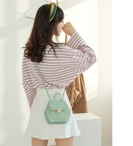 Light green hexagonal crossbody bag featuring decorative yellow stitching and gold buckle