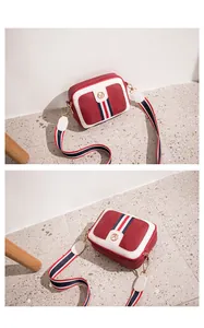 Close-up of wine red pebble leather camera bag with white piping and striped strap