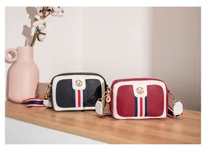 Detail of crossbody camera bags with striped straps and metal logo on wood shelf