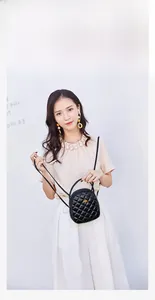 Detailed view of black quilted crossbody bag with gold bee emblem on model