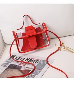 Detail view of mini transparent PVC crossbody bag with red leather trim on white sofa