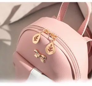 Detail of pink faux leather bag featuring golden leaf zippers and bow decoration
