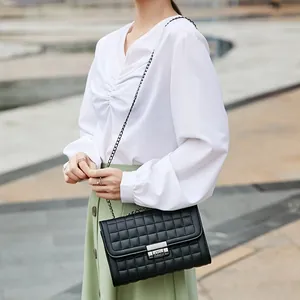 Sac à bandoulière noir matelassé pour femme avec chaîne et fermoir porté par un mannequin