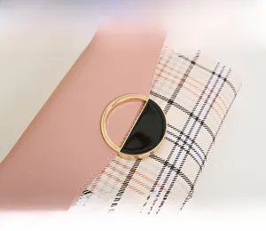 Close-up of pink leather and beige plaid bag with circular gold metal buckle detail