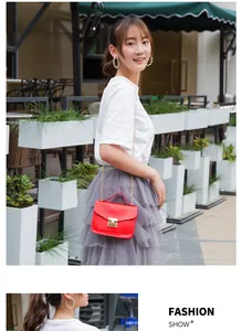Detail of red lizard-texture crossbody bag with golden clasp and metal chain strap