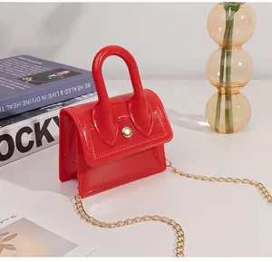 Close-up of a mini red jelly bag with a gold metal chain strap and a shiny finish