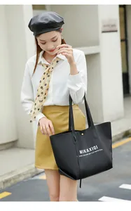 Detail of black tote bag with white lettering, gold snap closure and slender straps