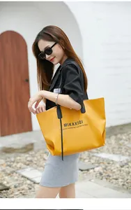 Detail of mustard yellow tote bag featuring contrast black straps and chic text print