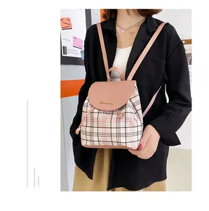 Detalle de mini mochila de cuadros rosa con solapa de cuero y logo dorado en una modelo