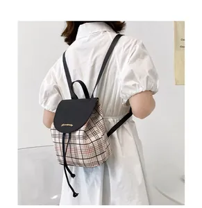 Detalle de mini mochila de cuadros con solapa de cuero negro llevada por una modelo