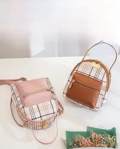 Close-up of mini plaid crossbody backpacks in pink and brown with front zipper details