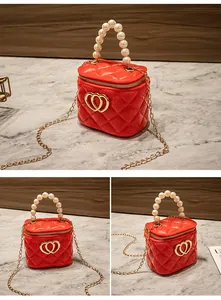 Mini borsa trapuntata rossa con manico di perle e chiusura a cuore dorata su tavolo