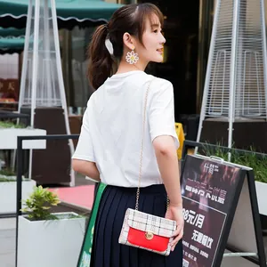 Chic plaid crossbody bag with red flap and chain strap worn by a model outdoors