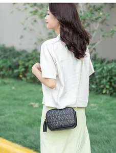 Outdoor shot of a black quilted crossbody bag with metal chain strap and tassel detail