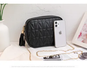 Detail of black quilted crossbody bag with gold chain and tassel next to a phone