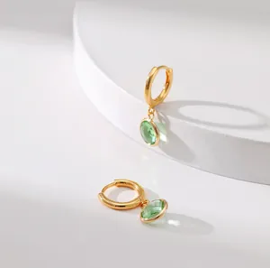 Detail shot of gold hoop earrings featuring clear green faceted zircon pendant drops