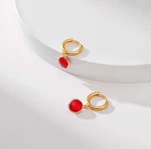 Macro shot of gold huggie earrings with round red gemstone pendants on white background