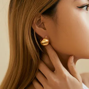 Close-up of golden hollow ball earrings with brushed texture on female model's ear