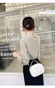 Détail du sac bandoulière matelassé blanc avec logo doré sur fond de robe noire élégante