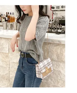 Detail of checkered crossbody bag with gold lock and chain strap in casual setting