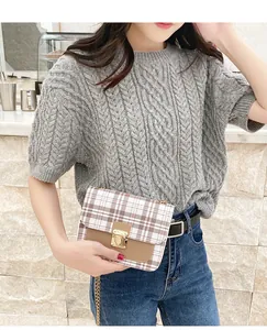 Close-up of a plaid crossbody bag with gold metal buckle and chain on a cable knit sweater