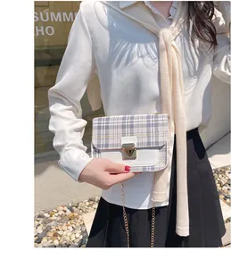Detail of plaid crossbody bag with gold metal clasp and chain strap on a model