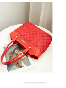 Détail du sac cabas matelassé rouge avec logo en métal doré et clous sur une table