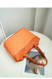 Détail du sac fourre-tout orange avec matelassage, rivets et logo sur une table blanche
