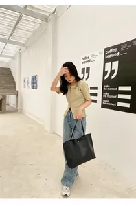 Outdoor street style view of a black crocodile pattern tote bag paired with a green knit top