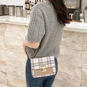 Plaid crossbody shoulder bag with gold chain and buckle shown on a model in a cafe