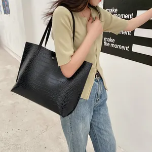 Black crocodile embossed tote bag with gold button closure carried by a model