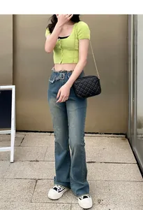 Chic model wearing a black quilted chain camera bag with a green cardigan and jeans