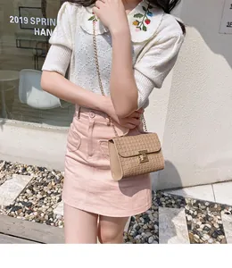 Detail view of beige textured small square bag with golden chain and metal turn-lock