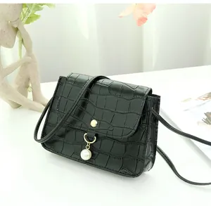 Detail of black crocodile texture bag with gold snap button and elegant pearl charm