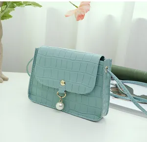 Close-up of light blue croc-effect square bag with pearl pendant and gold hardware