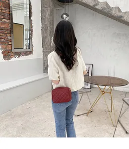 Detail of red quilted crossbody camera bag with gold chain strap on female model