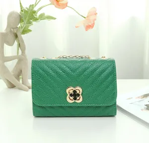 Detail of green quilted leather bag featuring a gold clover clasp and metallic chain