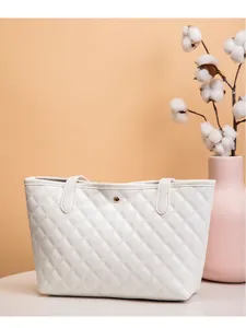Détail d'un sac cabas blanc matelassé avec boucle dorée sur fond de couleur pêche pastel