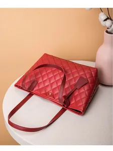 Détail du sac cabas en cuir rouge matelassé avec rivet doré sur une table en marbre