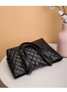 Gros plan du sac cabas matelassé noir avec emblème doré sur du marbre