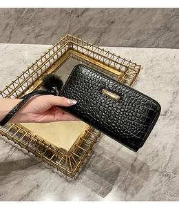 Close-up of black crocodile pattern wallet with gold metal plate and plush pompom charm
