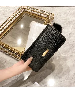 Detail of crocodile pattern leather wallet with gold metal bar and faux fur pompom charm