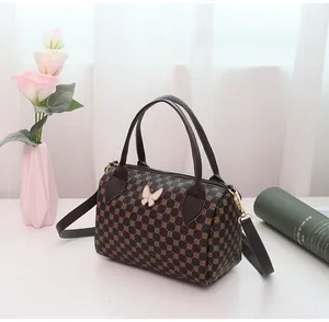 Close-up of brown Boston bag with geometric floral patterns and butterfly charm